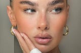 A clean looking woman with clear skin, glossy lips, slicked back hair, and gold hoop earrings.