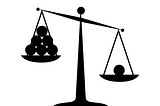 Image of a scale. One side has one ball and is weighed down. The other side has five balls and is not weighed down as much.