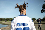 A photograph of the backside of Justin Bieber showcases his two dreadlocks, tied into two pigtails. He’s wearing a football jersey.