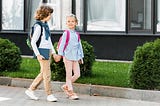 Boy and girl with backpacks walking on sidewalk