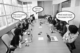 A team meeting on a large rectangular desk with roughly 20 colleagues on either side asking questions on the objective.