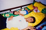 An analogue photograph of me and my dad. We were lying on a bed (covered with a yellow bed sheet), smiling to the camera.