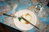 um prato branco com comida e taças de água sobre uma toalha de mesa estampada
