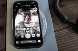 Photo of an iPhone open to the TikTook app, resting on a book. The app has pulled up a photo of a man wearing a hat and glasses who is making a cutting motion at his neck.