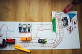 Toy vehicles set up over a child’s drawings of roads.
