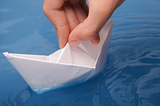 A paper boat being set afloat in blue water