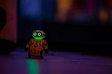 A small yellow robot toy with little wheels and bright eyes in the dusk on a table.