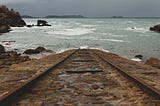 Image of an old railroad track that runs  into a body of water and disappears.