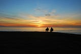 A couple sitting in camping chairs watching the sun set over the sea