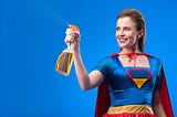 portrait of cheerful superwoman with detergent in hand isolated on blue