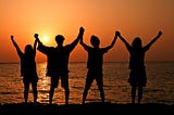 Friends holding hands near the ocean at sunset