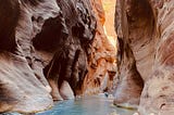 two people walking through water in between a canyon