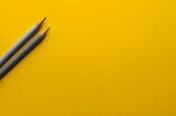 Two grey pencils on a yellow surface