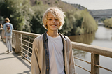 A happy teenage boy standing on a bridge over a river.