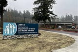 A photo of the residential treatment center at Maple Lane, with a sign that is branded with the Washington State Department of Social and Health Services, its logo and a new one-story building with trees in the background.