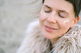 A young woman with glitter on her cheeks smiles gently with closed eyes