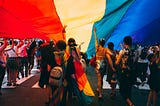 A crowd of people walks beneath a rainbow flag at Pride.