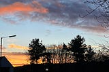 Pink, grey and orange clouds in the sky behind some trees