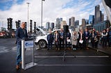 The governor speaks to a crowd with the Seattle skyline in the background.