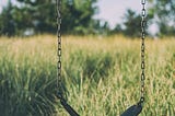 A black swing connected to a chain link hangs in a an empty field of grass