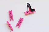 4 pink clothes pegs randomly placed and a red bottom stiletto shoe placed on top of one peg