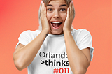 A woman holding her cheeks. She seems very surprised. She wears a shirt with the title logo “Orlando thinks #011” printed on it.