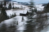 a snow-covered house is visible in the midst of blurred trees