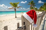 An image of a Hawaiian beach on a sunny day with a Santa hat propped on a wooden fence