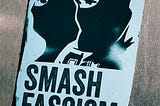 A black-and-white poster on a concrete wall shows two figures in balaclavas and the legend SMASH FASCISM.