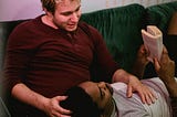 A man reading and resting his head on another man’s lap.