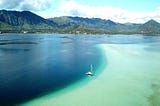 A sailboat anchored in a bay of green and blue waters.