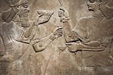 Stone relief of 2 Sumerian Gods facing each other and holding a cup and tools
