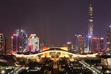 The cityscape of Shenzhen at night, with a purple black background sky and buildings with white and yellow lights.