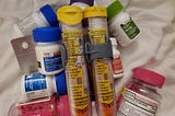 An EpiPen next to bottles of antihistamine drugs on a white sheet