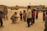 Man in military uniform shakes hands with Iraq children
