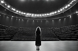 A black and white picture of a woman on an empty stage facing an empty audience