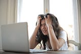Young woman in white T-Shirt sitting at her laptop showing frustration