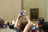 A group of tourists taking pictures of the Mona Lisa with their phones.