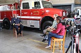 Three young adults sit down with Oakland Fire Chief Reginald Freeman at a local fire station.