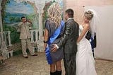 The bride standing on the right looking where her husbands left hand is at a photo shoot.