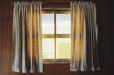 A closed window with curtains spread apart.