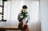 A black woman with a bouquet of flowers hiding her face.