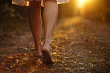 Young girl legs walking barefoot through a forest toward the sunset. It represents the innocence of a young girl stepping into the dangerous vicious cycle of dieting and emotional eating for the first time.