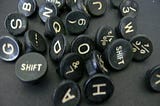 about 25 round keys from a typewriter (with letters, numbers, and punctuation on them) that have been removed from the typewriter and are lying randomly on a black surface