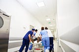 Hospital staff rush a patient down a hospital hallway on a gurney.