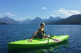 Woman on a boat in water against a backdrop of mountains and sky