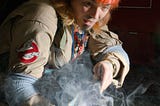 A man in Ghostbuster cosplay holding a smoking ghost trap. The dynamic side lighting casts a strong shadow on the subject and smoke.