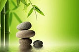 Four flat stones on top of each other next to a single smaller stone near a bamboo shoot against a green background.