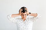 A stressed woman with dark hair holds her head in between her hands in a sign of frustration.