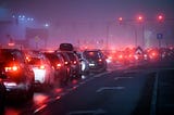 Traffic lights and a long queue of cars with their rear lights on contrast with the dim murky background. Buffalo, Niagara.